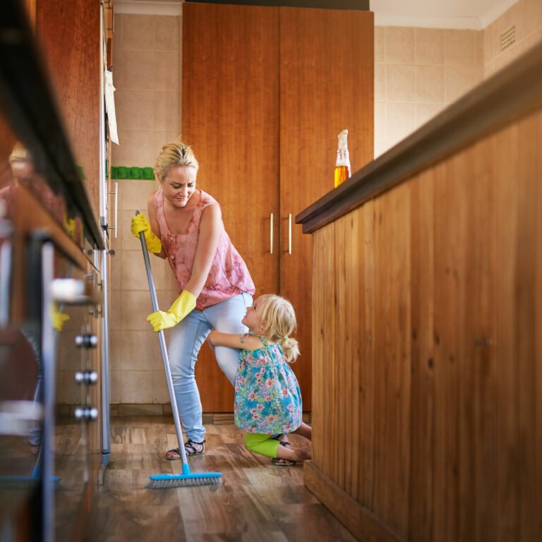 Shot of a little girl holding onto her mothers leg while she sweeps a kitchen.